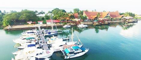 A marina with several boats docked, surrounded by buildings with red roofs and palm trees.