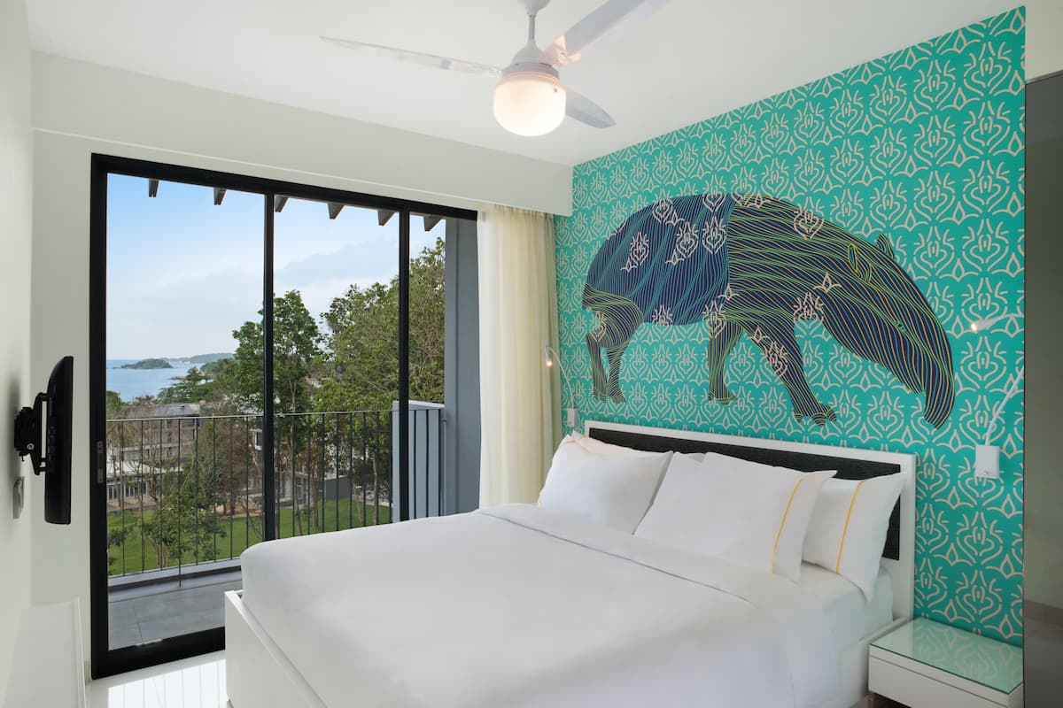 A bedroom with a large bed, a ceiling fan, a view of the outdoors, and a patterned wall.
