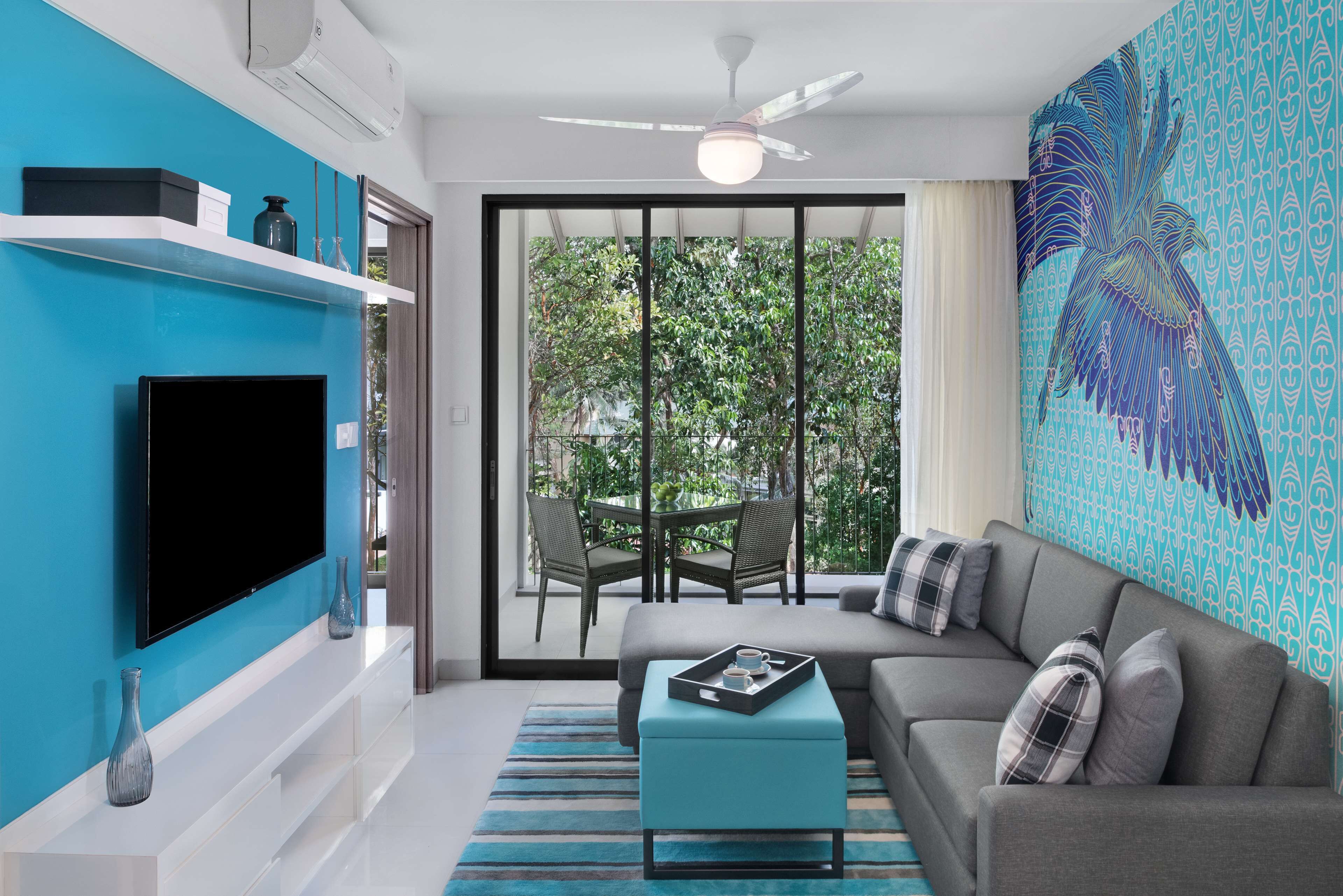 A modern living room with a flat-screen TV, a sofa, a coffee table, and a balcony with a view of greenery.