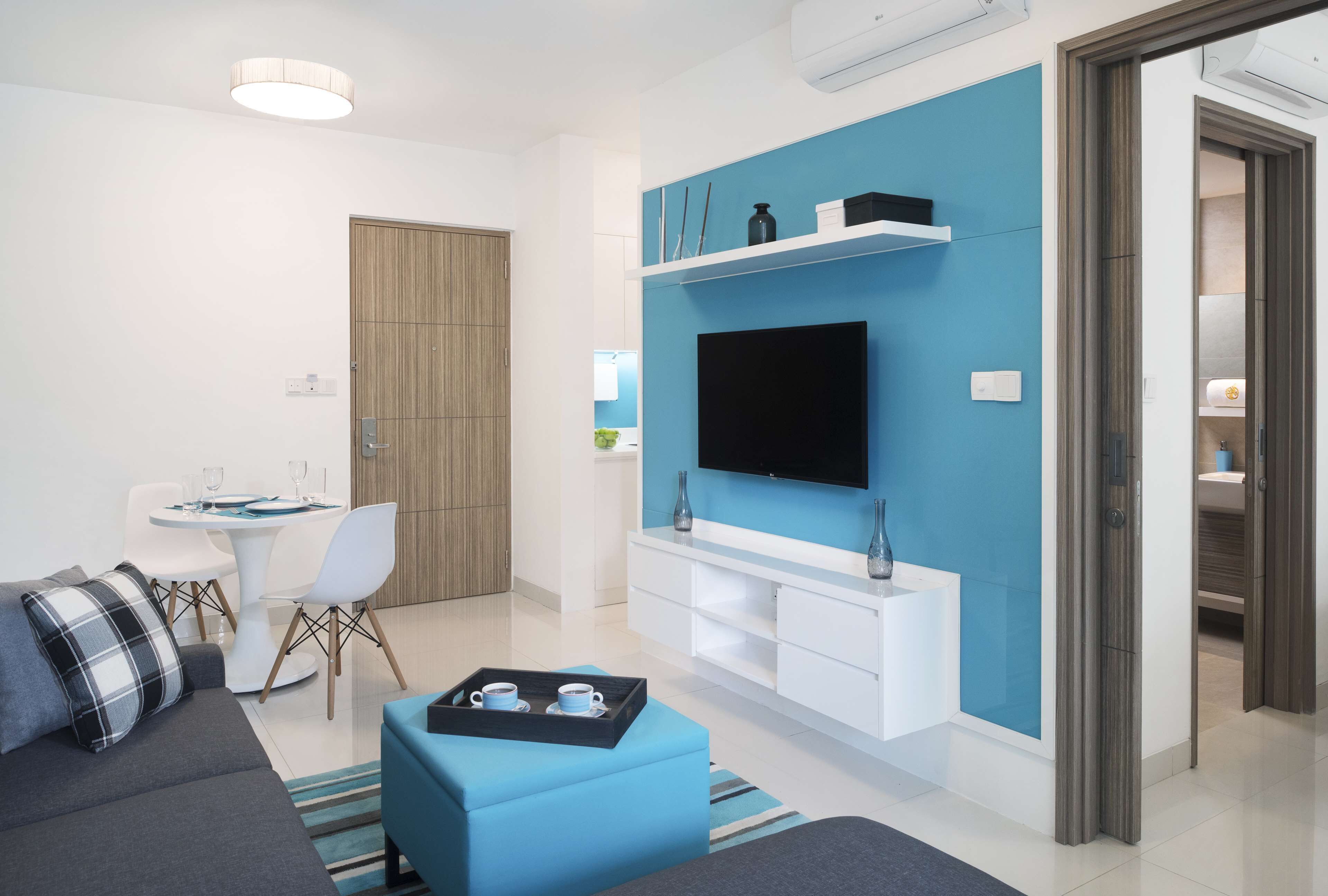 Una sala de estar moderna con televisor de pantalla plana, un comedor con mesa y sillas blancas, y una pared azul de acento.