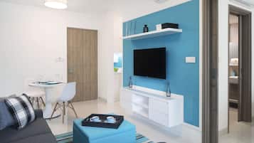 Uma sala de estar moderna com televisão de tela plana, área de jantar com mesa e cadeiras brancas e uma parede azul decorativa.