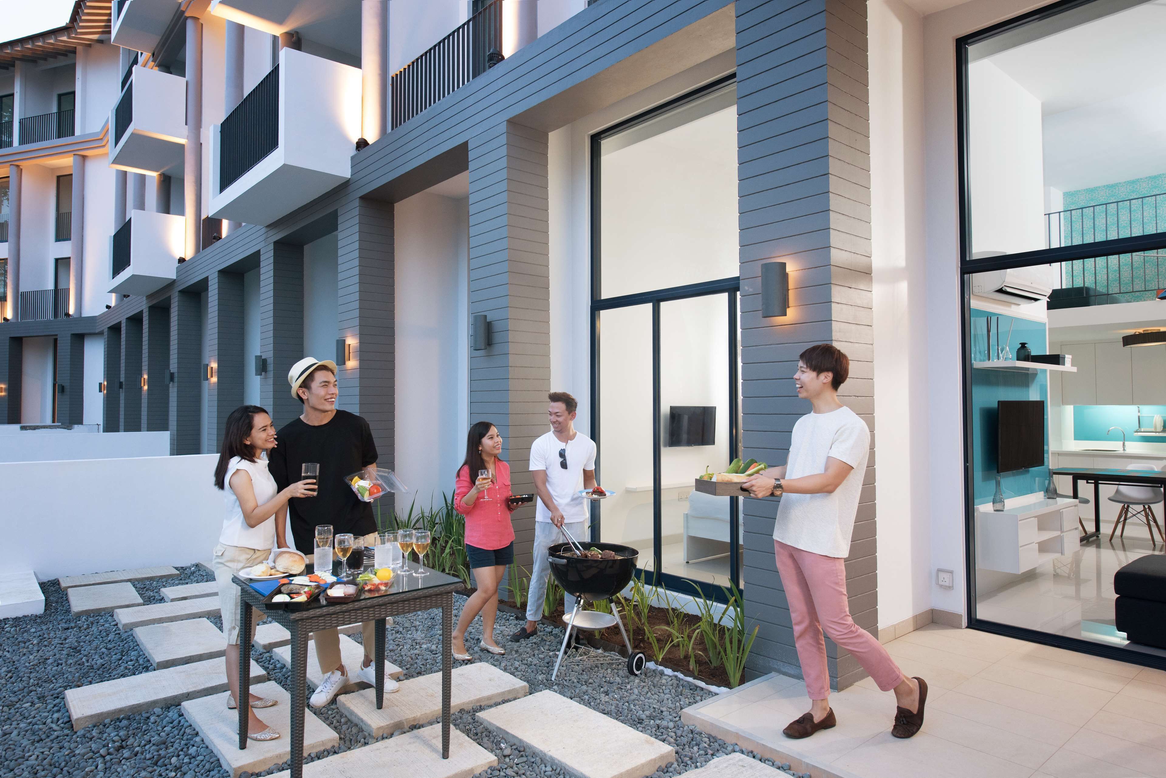 A modern outdoor dining area with a grill, a table with food and drinks, and a kitchen visible through a glass door.