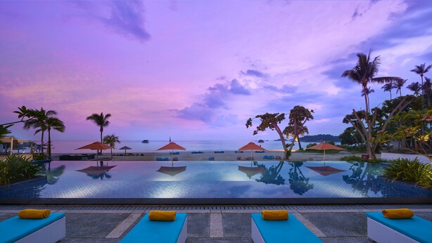 A poolside area with lounge chairs and umbrellas, overlooking a beach and ocean at sunset. - Cassia Bintan, part of Banyan Group (Bintan)