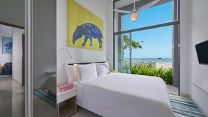 A modern hotel room with a large bed, a nightstand, a painting of a horse, and a view of the beach. - Cassia Bintan, part of Banyan Group (Bintan)