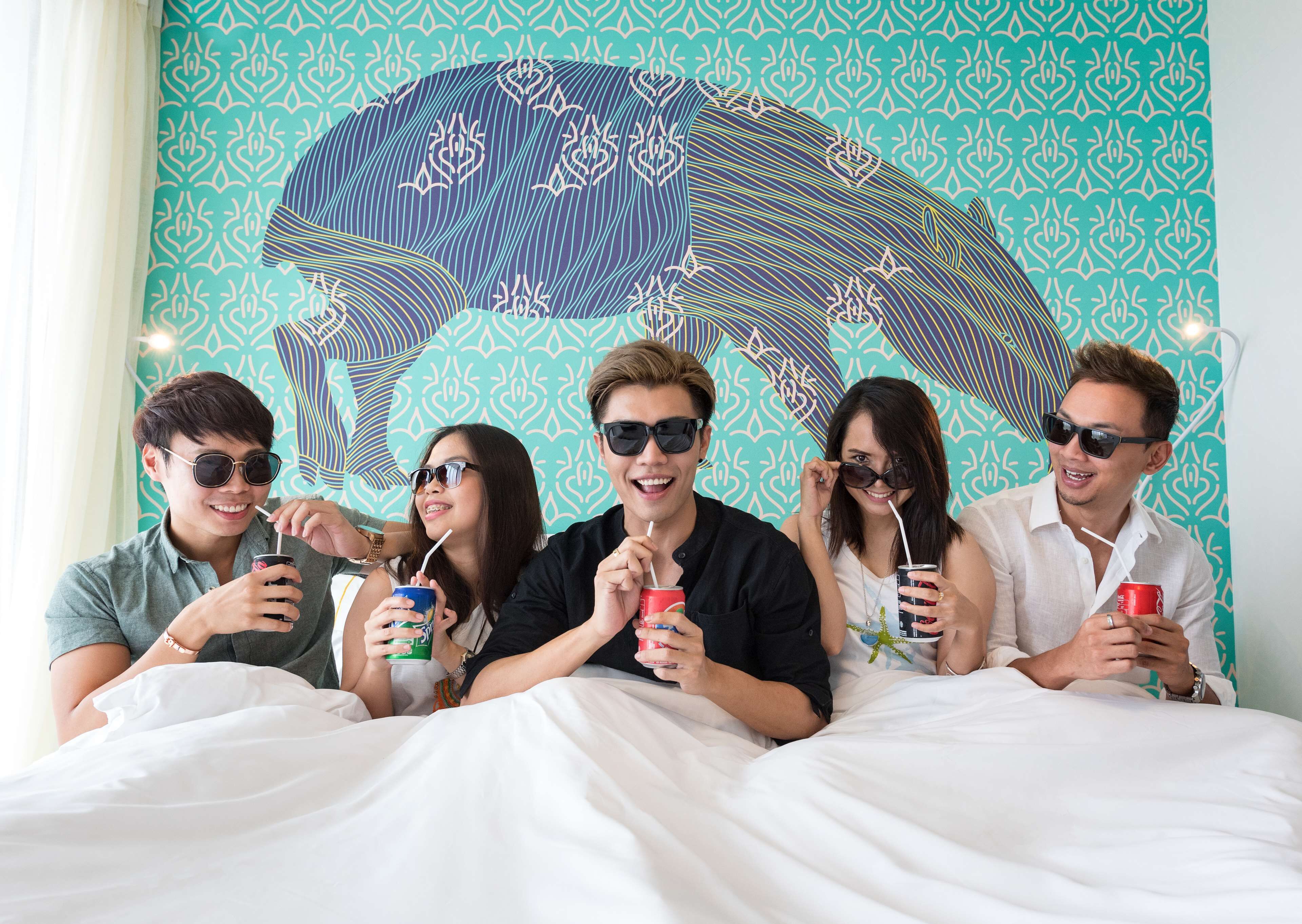 A group of people sitting on a bed with a patterned wall behind them.