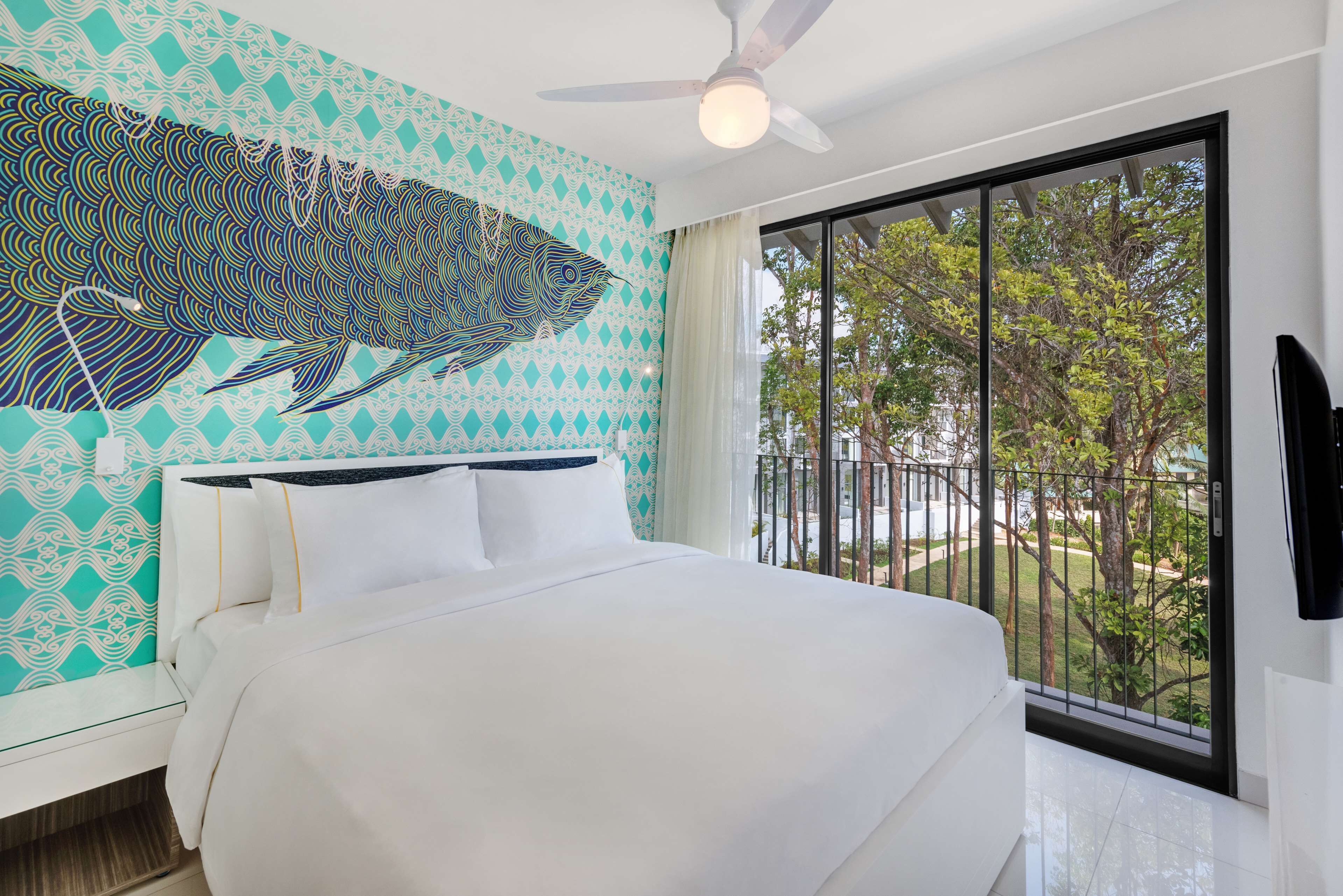 A bedroom with a large bed, a ceiling fan, and a view of the outdoors through a sliding door.