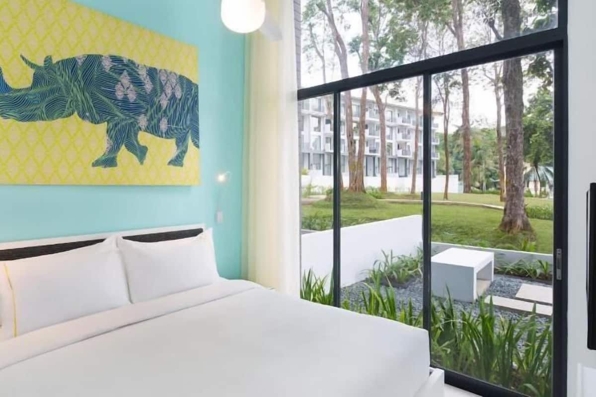 A modern hotel room with a large bed, a window with a view of the outdoors, and a wall with a geometric pattern.