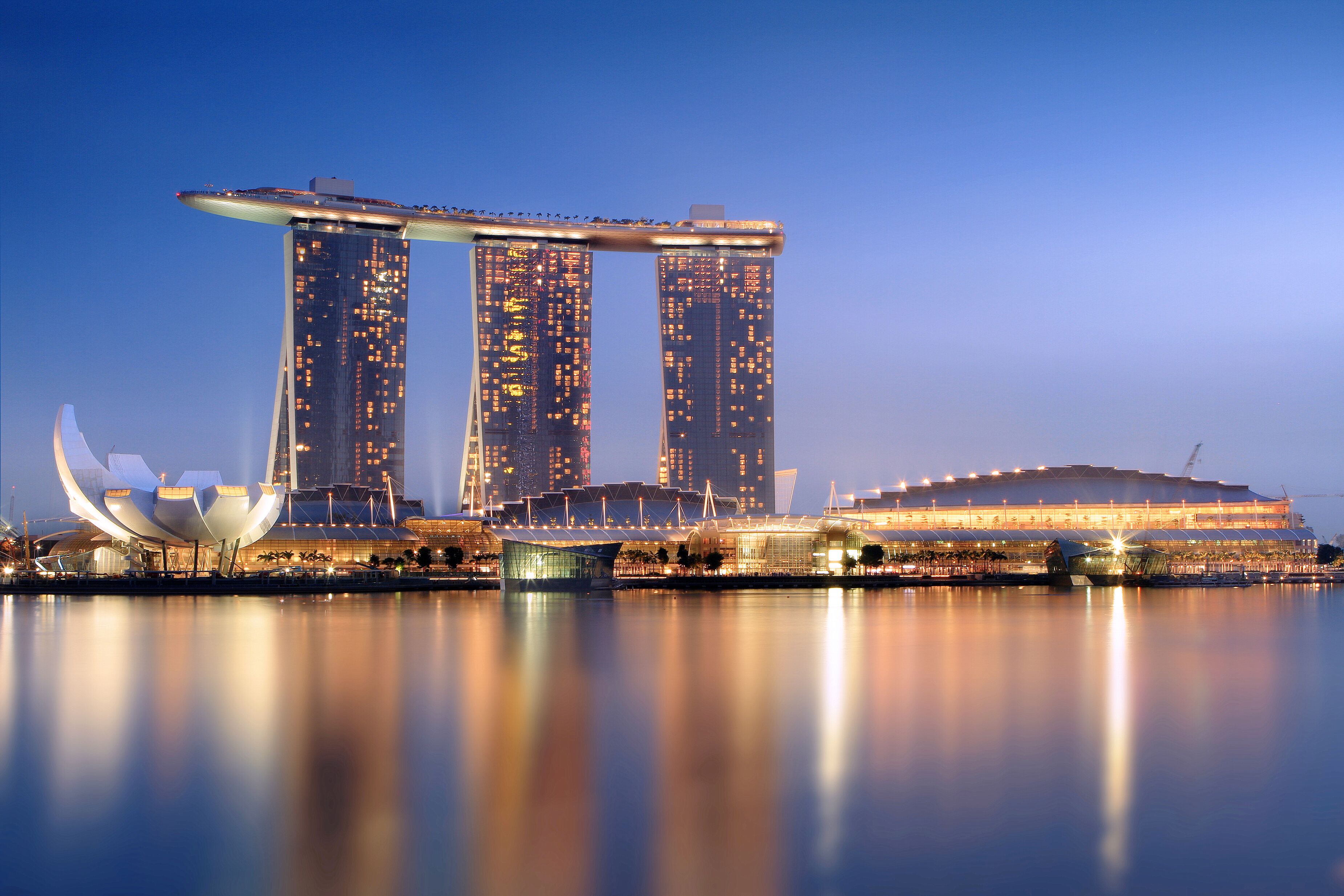 A waterfront view of a modern building complex with a distinctive cantilevered structure and a large stadium.