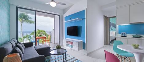 Una sala de estar moderna con un sofá, una mesa de centro y un televisor. Cuenta con un balcón con vista al océano.
