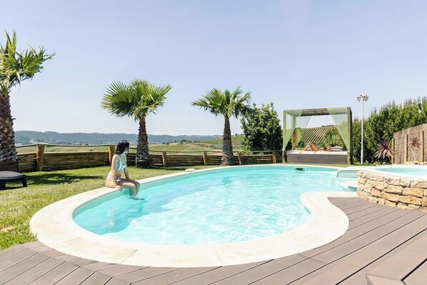 A swimming pool with a wooden deck, palm trees, and a stone wall.