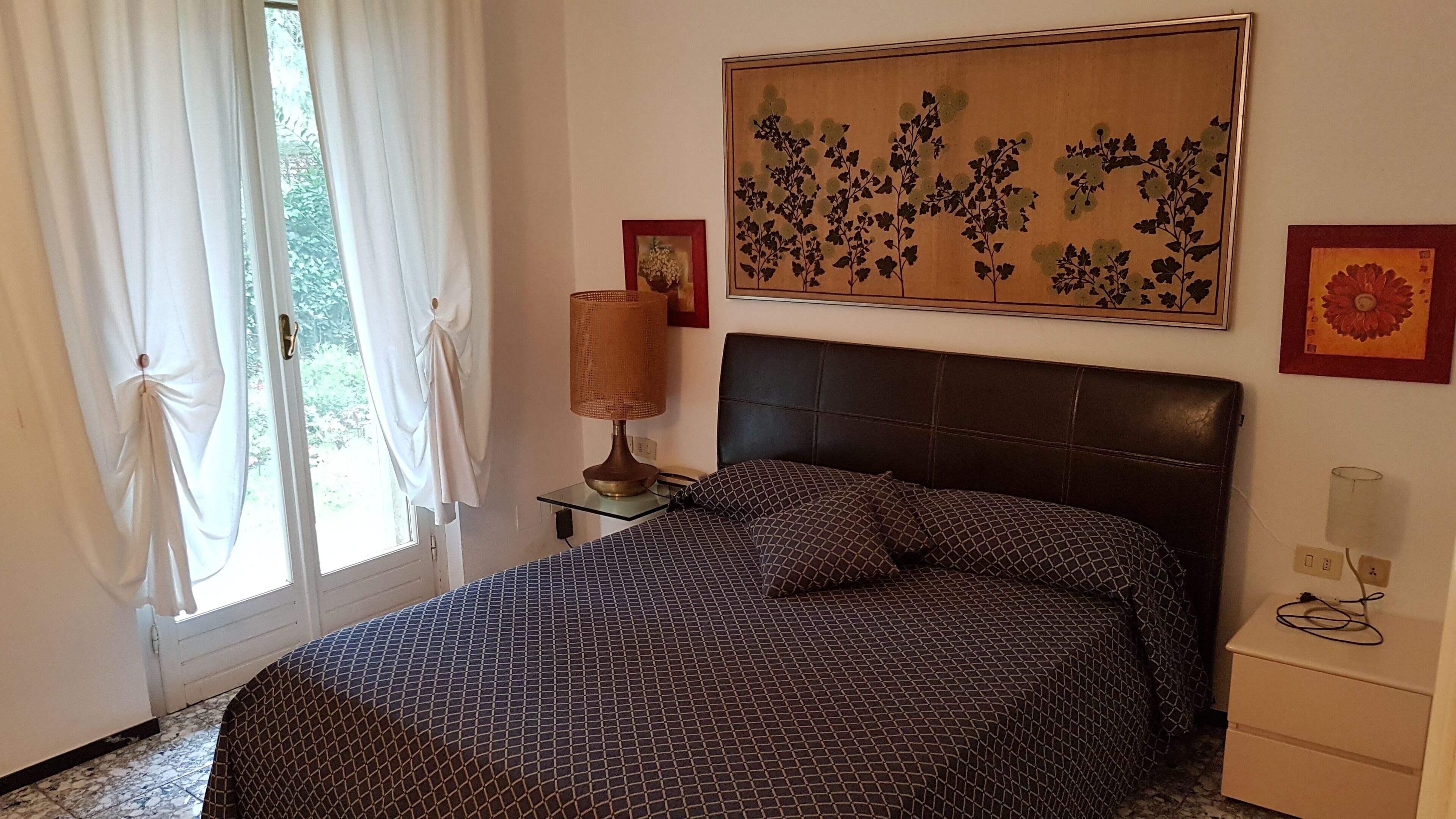 Un dormitorio con cama, mesita de noche, lámpara y una obra de arte colgada en la pared.
