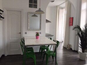 Un comedor con una mesa blanca, sillas verdes, un florero con flores rosas, un espejo y un letrero que dice 'KEEP CALM AND CARRY ON'.