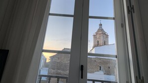 Une vue à travers une fenêtre à cadre blanc, révélant un bâtiment doté d’un clocher et d’une croix au sommet, ce qui laisse supposer qu’il s’agit d’un édifice religieux ou historique.