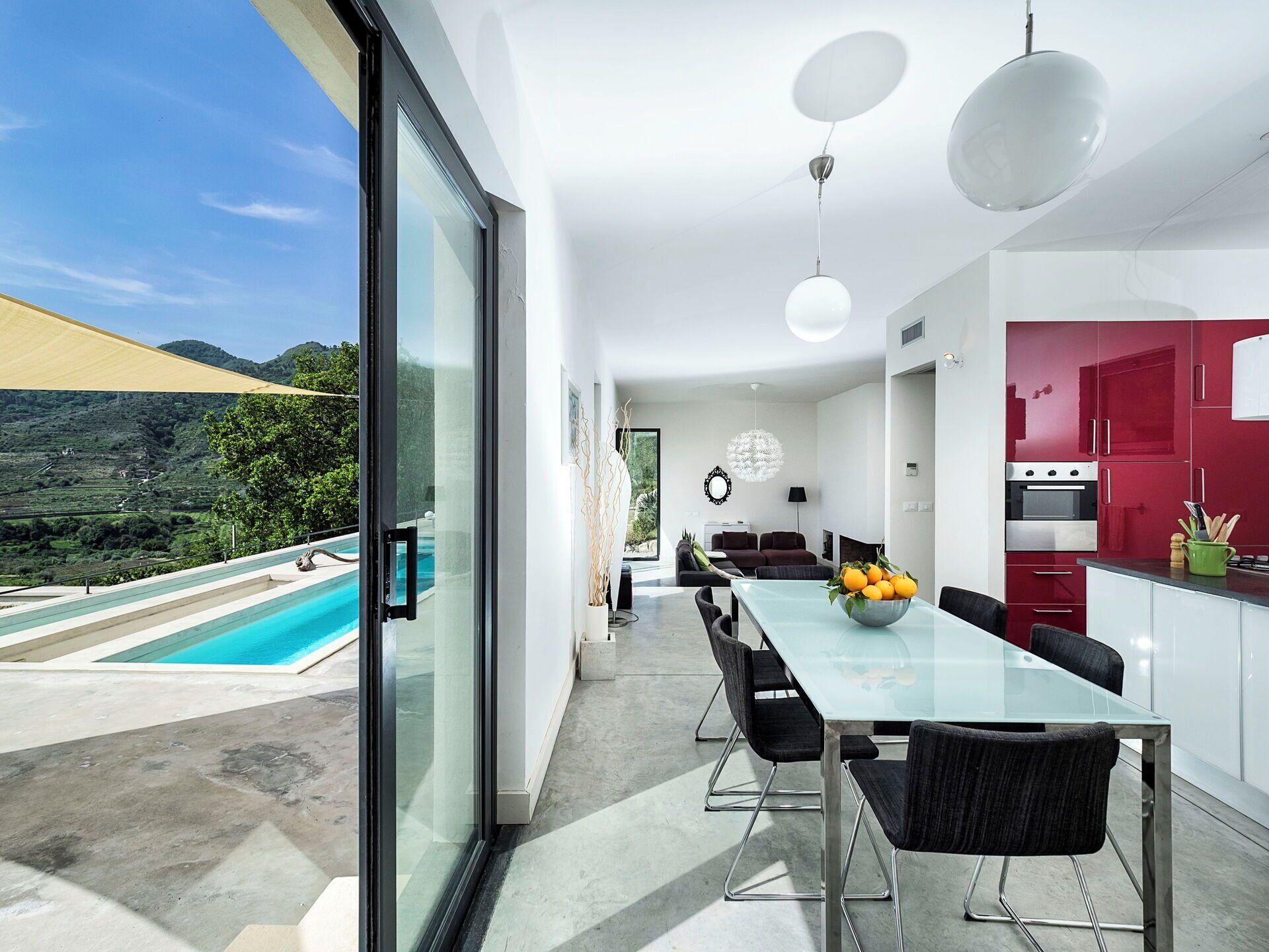 Una cocina moderna con armarios rojos, un comedor con mesa de vidrio y vistas a una piscina.