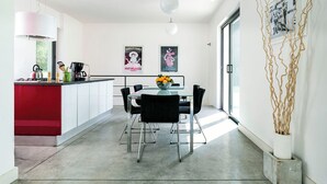 Una cocina moderna con una pared de acento roja, un comedor con una mesa de vidrio y sillas negras, y dos carteles enmarcados en la pared.