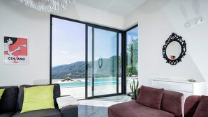 Una sala de estar moderna con un sofá gris, un sofá rojo y un ventanal de vidrio que da a una piscina.