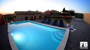 A swimming pool with lounge chairs, a small garden, and a building with a tiled roof.