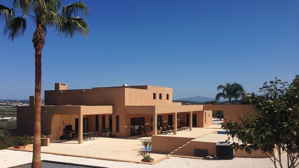 A modern building with a flat roof and multiple rooms, surrounded by a gravel courtyard and palm trees. - Amazing Villa - Lagos (Lagos)