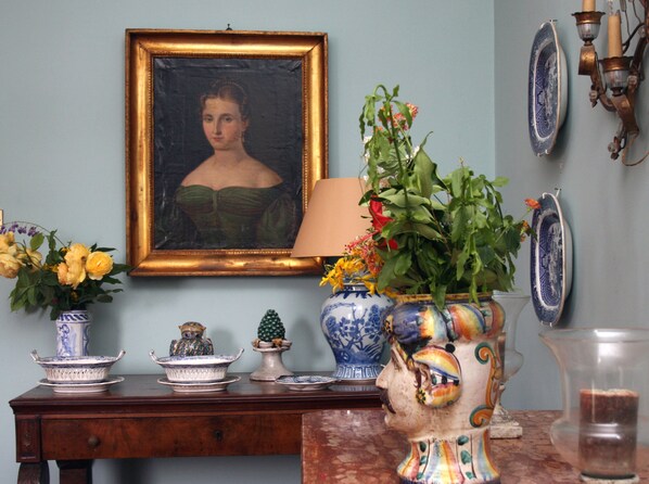 Una habitación con un aparador de madera, un retrato enmarcado y varios objetos decorativos, como jarrones y una figurina de cerámica.