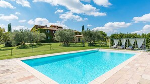 Une piscine rectangulaire bordée de pierres, entourée d’une pelouse bien entretenue et d’une maison dont le toit est recouvert de tuiles.