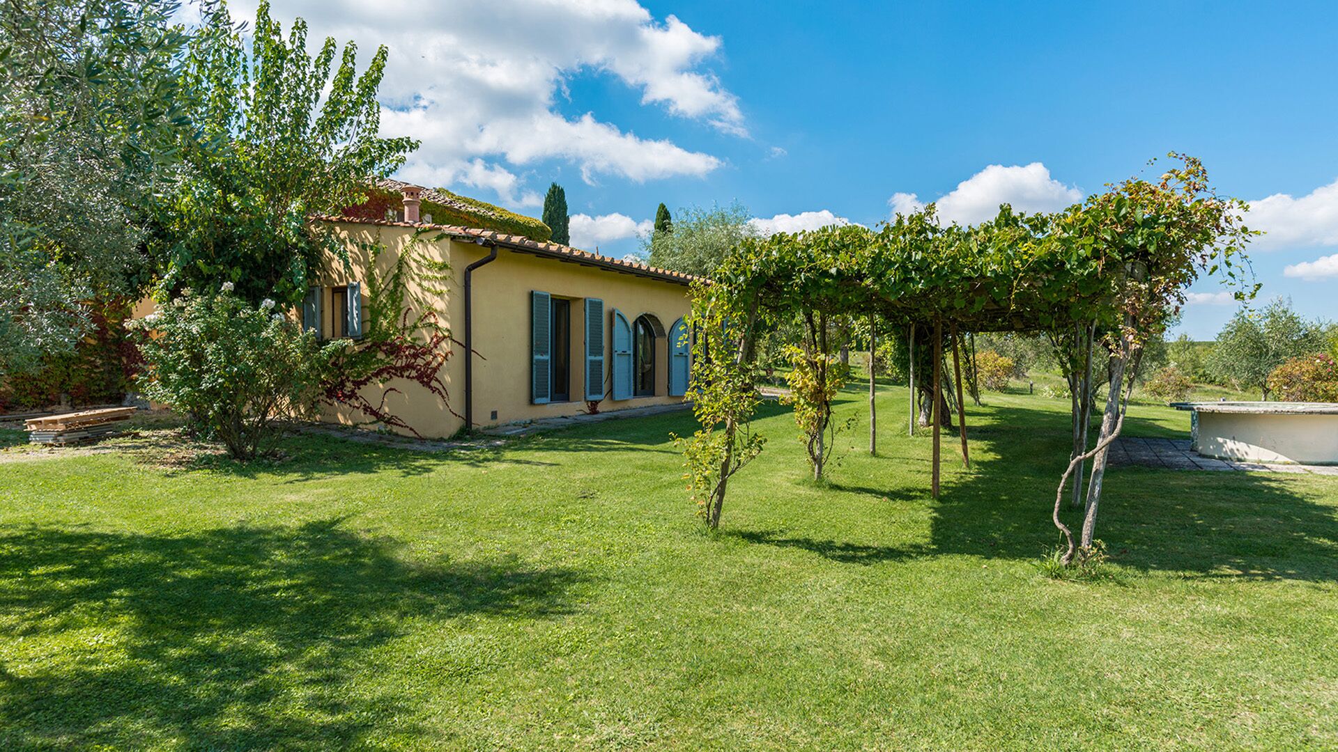 A villa with a garden, a pergola, and a clear blue sky.
