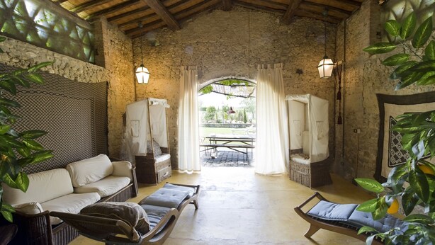 Une pièce rustique avec un mur en pierre, un plafond en bois, un canapé, deux fauteuils, une table et un lit à baldaquin.