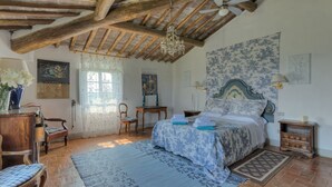 Une chambre avec un plafond en bois, un lit recouvert d’une couvre-lit à motifs floraux, un lustre et une grande tapisserie florale accrochée au mur.
