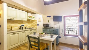 A compact kitchen with white cabinets, a microwave, a sink, and a dining table with chairs. - Studio Cavour (alghero)