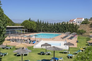 A pool area with lounge chairs and umbrellas, surrounded by greenery and buildings in the background. - Magnificent apartment very close to Lagos`s Marina (Lagos)