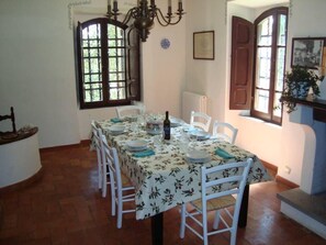 A dining room with a table set for four, white chairs, a floral tablecloth, and a chandelier. - The charming Villa Passo del Lupo - Agello/Solomeo (Agello di Magione)