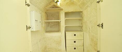 Una habitación pequeña y estrecha con una pared blanca, un estante de madera, un armario blanco y una puerta con pomo metálico.