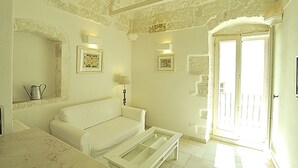 A room with a white sofa, a glass-top coffee table, a metal pitcher on a shelf, and a door leading outside. - CASA ROMA HISTORIC CENTER WIFI (Ostuni)