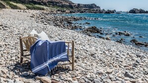 A beach chair with a blue towel on a rocky shore with a view of the sea and distant hills. - The Old Beach House - A house by the sea to reconnect with yourself (Keramoti western crete)