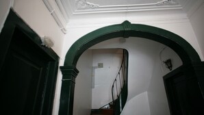 Un escalier orné d’une arche verte, avec des murs blancs et une main courante en bois.