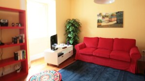 Un salon avec un canapé rouge, un meuble TV blanc, une bibliothèque et une plante en pot.