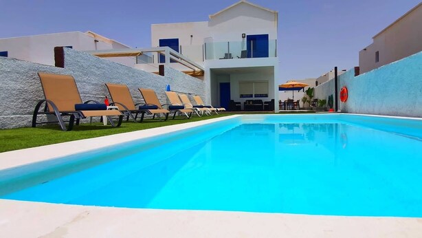 Una piscina con sillones de descanso y un edificio con balcón.