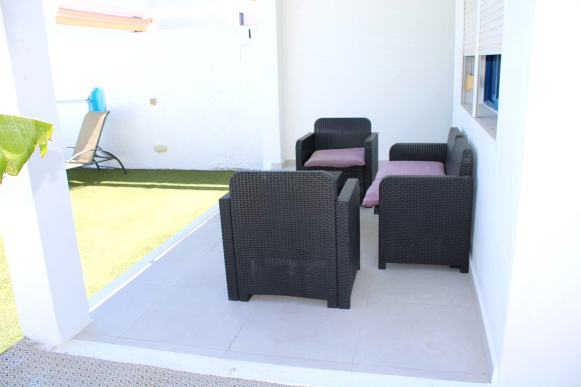 A patio area with two wicker chairs and a small table, a white wall, and a green lawn visible through an open door.