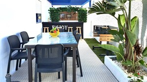 Un área de comedor al aire libre con mesa y sillas, una pared decorativa con un letrero que dice 'BEER' y una parrilla.