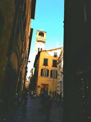 A narrow street with buildings on either side, a clock tower, and people walking.