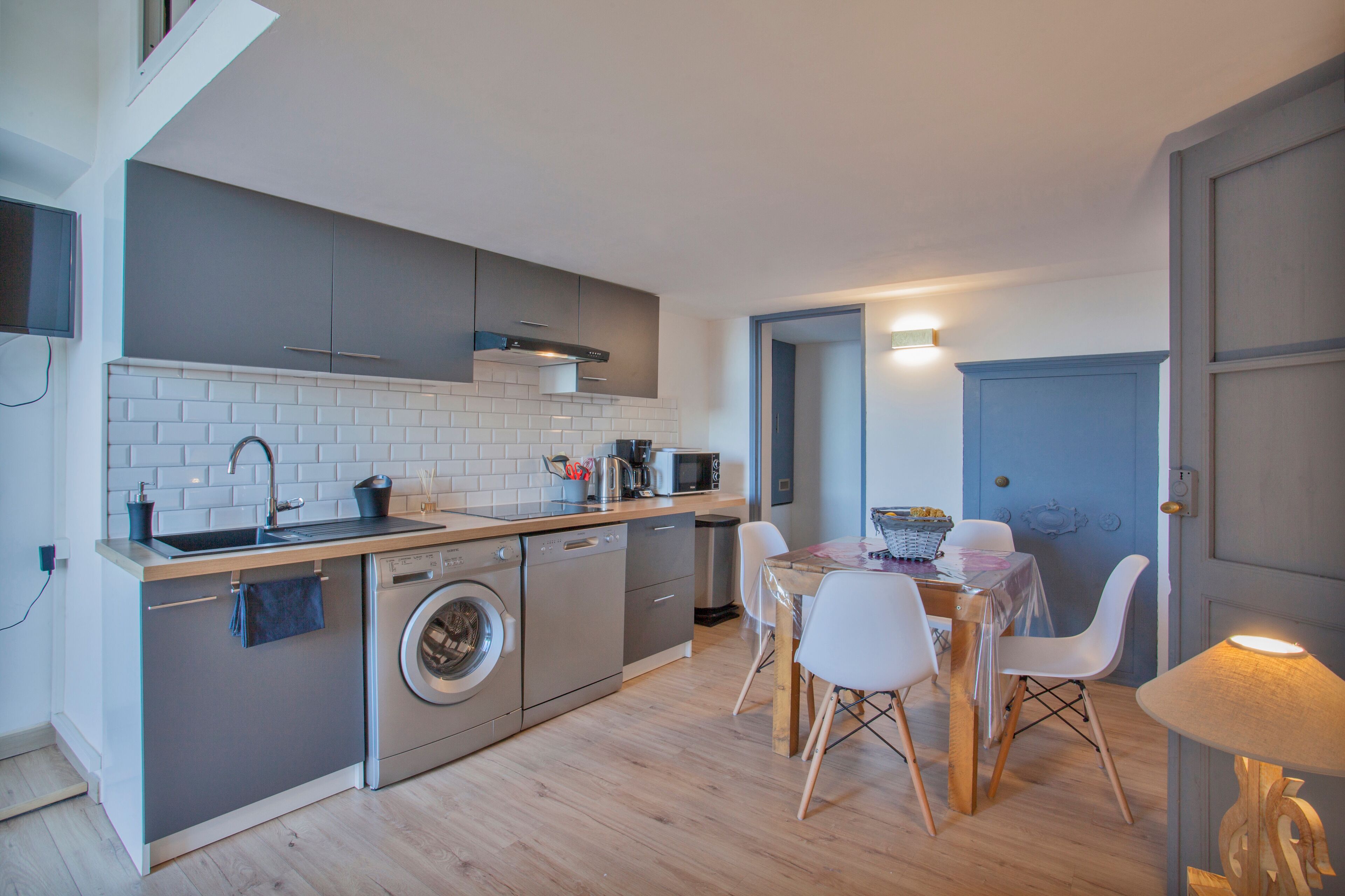 A compact kitchen with a washing machine, a microwave, and a sink. There's a dining area with a table and chairs.