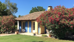 Ein traditionelles Haus mit Ziegeldach, blauen Türen und einem Garten mit blühenden Sträuchern.