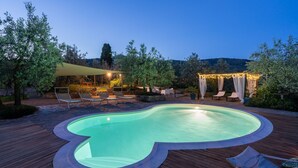 En swimmingpool med træterrasse, liggestole og en pergola med lyskæder.
