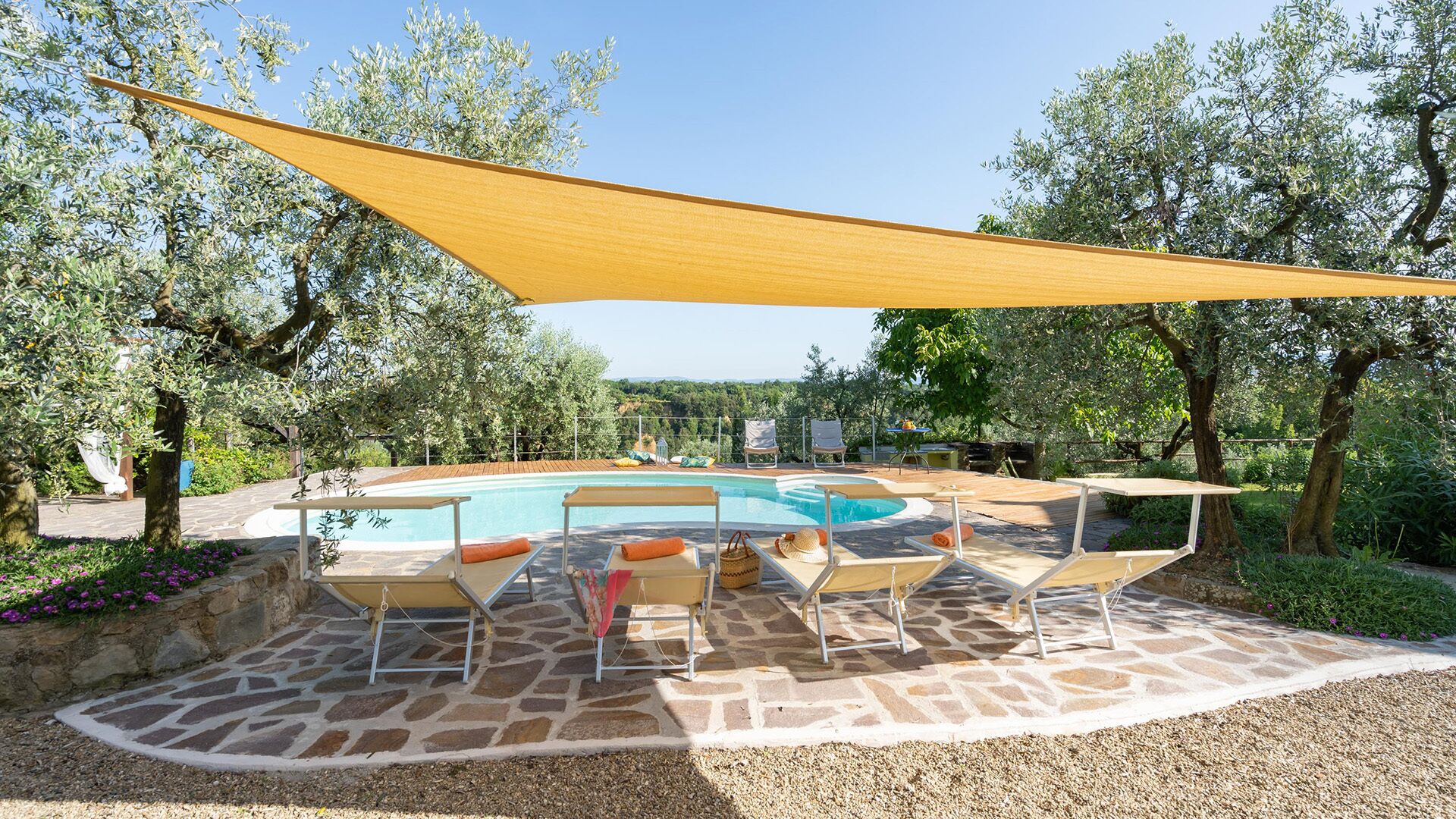 Ein Poolbereich mit einer Steinterrasse, Liegestühlen und einem gelben Sonnensegel.