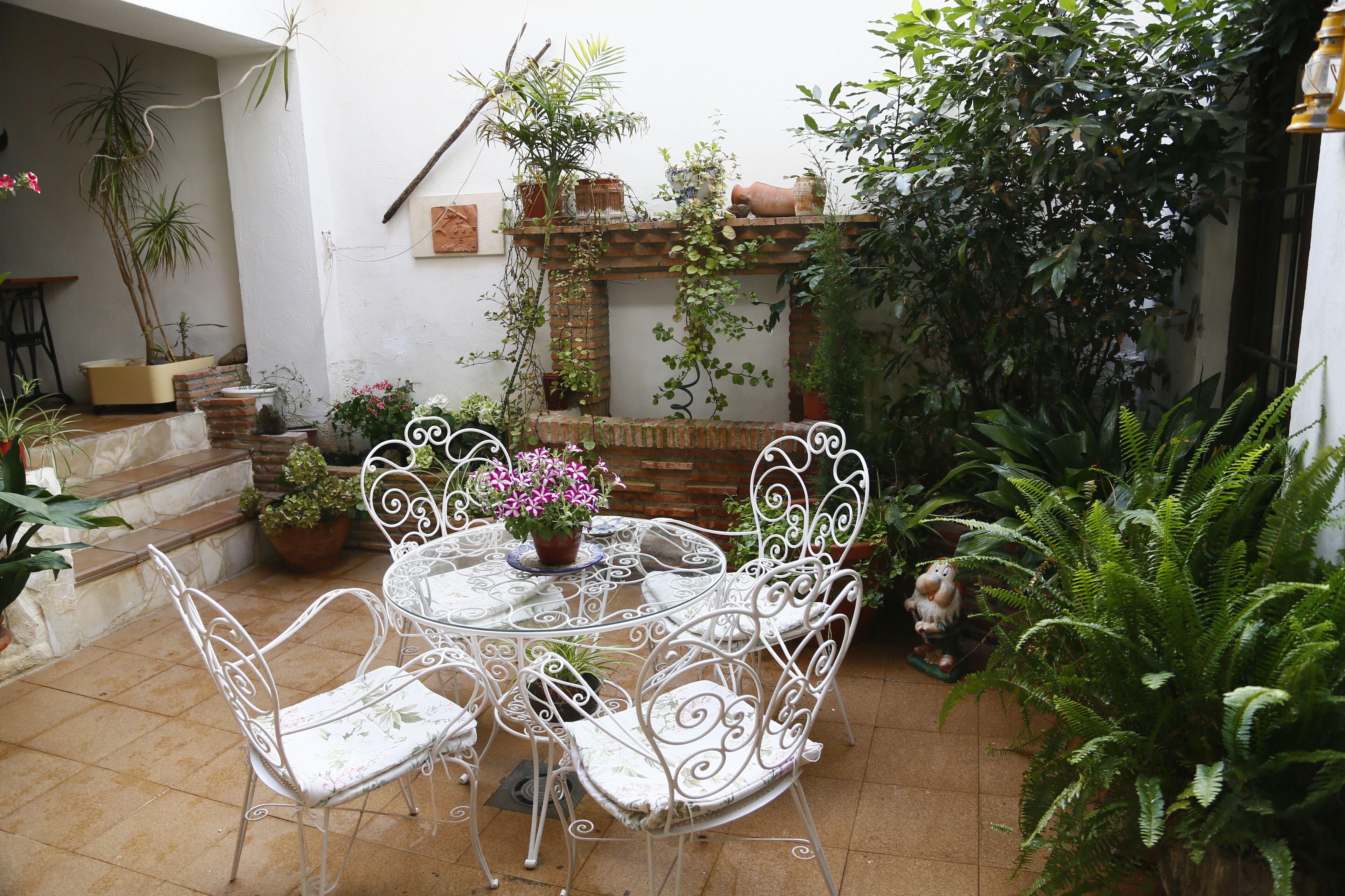 Eine Terrasse mit einem runden Tisch und weißen Metallstühlen, umgeben von Kübelpflanzen und einer Backsteinmauer.