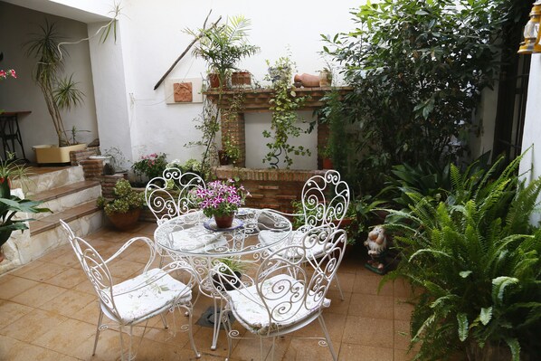 A patio with a round table and white metal chairs, surrounded by potted plants and a brick wall.
