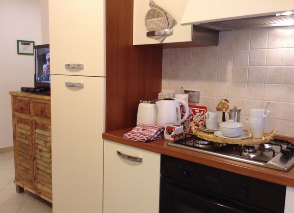 A compact kitchen with a stove, coffee maker, and a small cabinet.