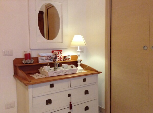 A bathroom with a wooden vanity, a mirror, a white cabinet with drawers, a small table with a lamp, and a red candle.