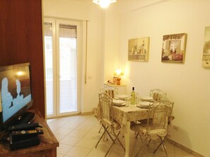 Un coin repas avec une table dressée pour quatre personnes, un téléviseur posé sur un meuble en bois et une porte donnant sur un balcon.