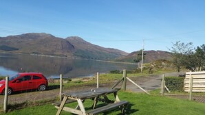 Ein Picknicktisch und ein rotes Auto in der Nähe eines Sees mit Bergen im Hintergrund.