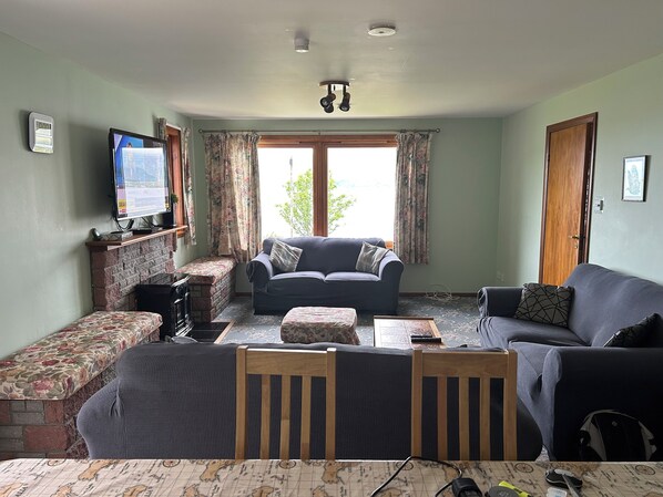 A living room with a sofa, a small table, and a television on the wall. - Glenelg - Detached House With Stunning Views Over the Sea to the Isle of Skye (Glenelg)